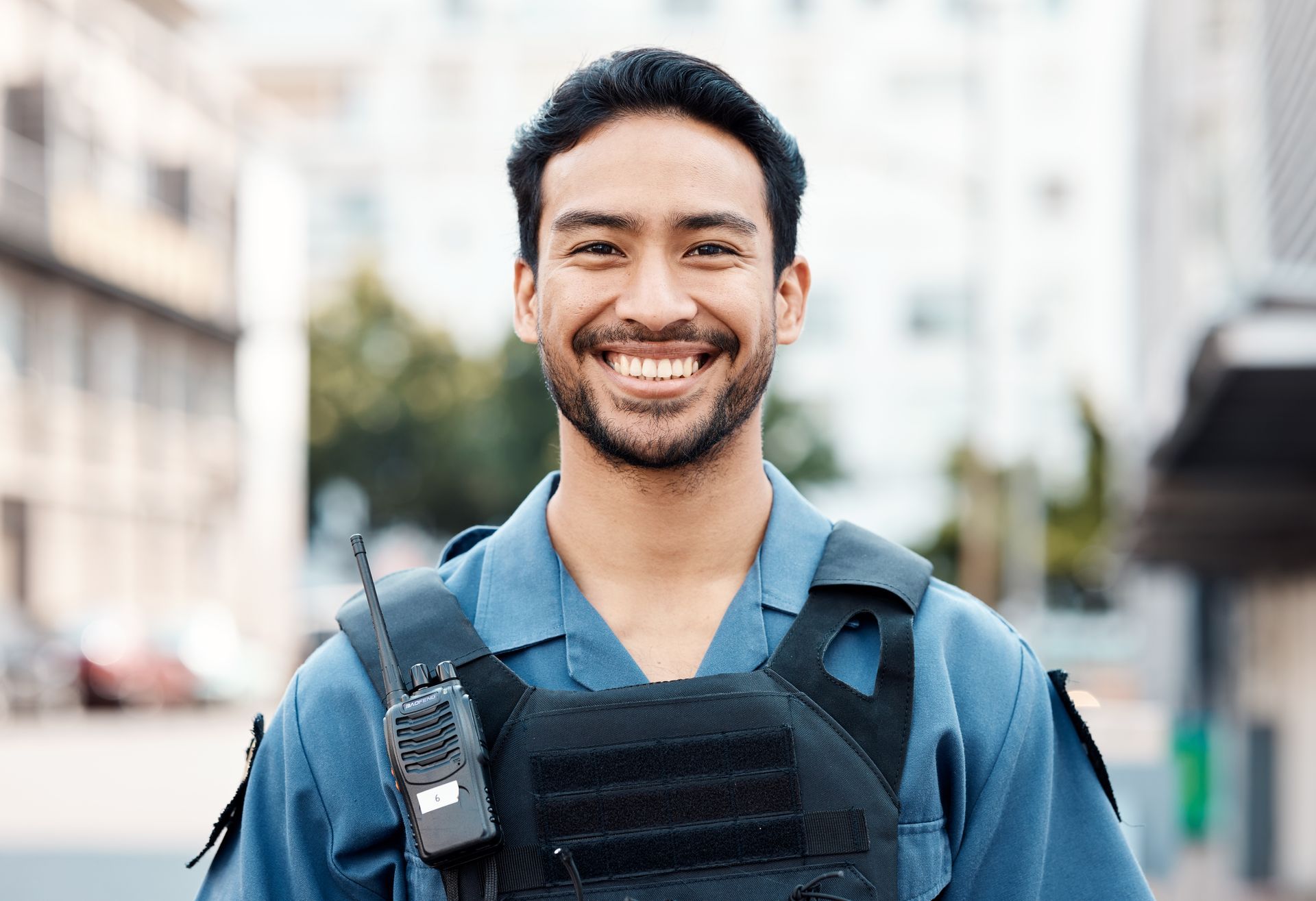 A man in a police uniform is smiling and holding a walkie talkie.