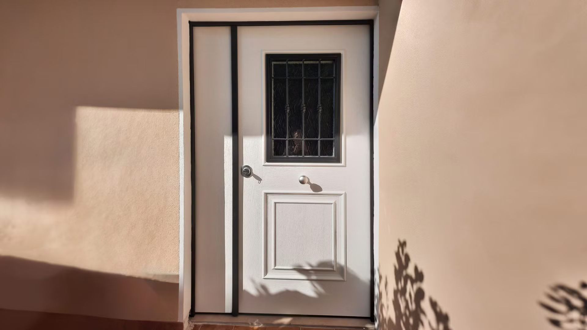 Una porta bianca con una finestra nera sul lato di un edificio.