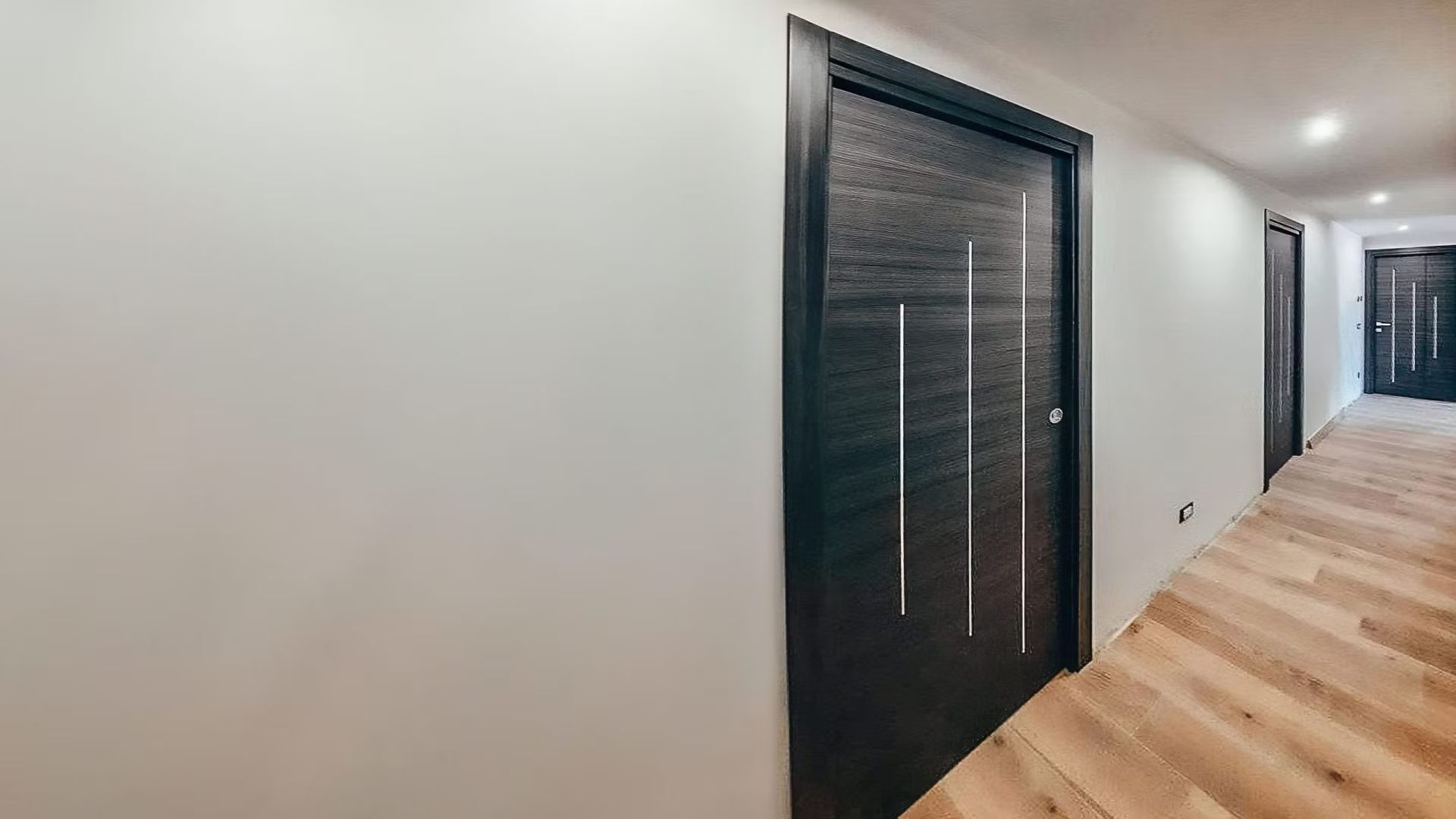 Un corridoio con una porta nera e pavimenti in legno.