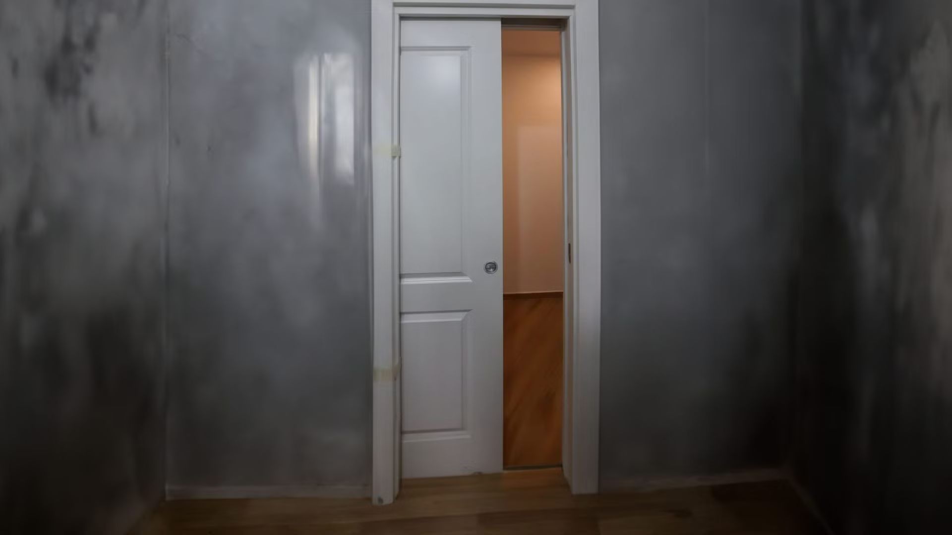 Una stanza vuota con una porta bianca e un pavimento in legno.