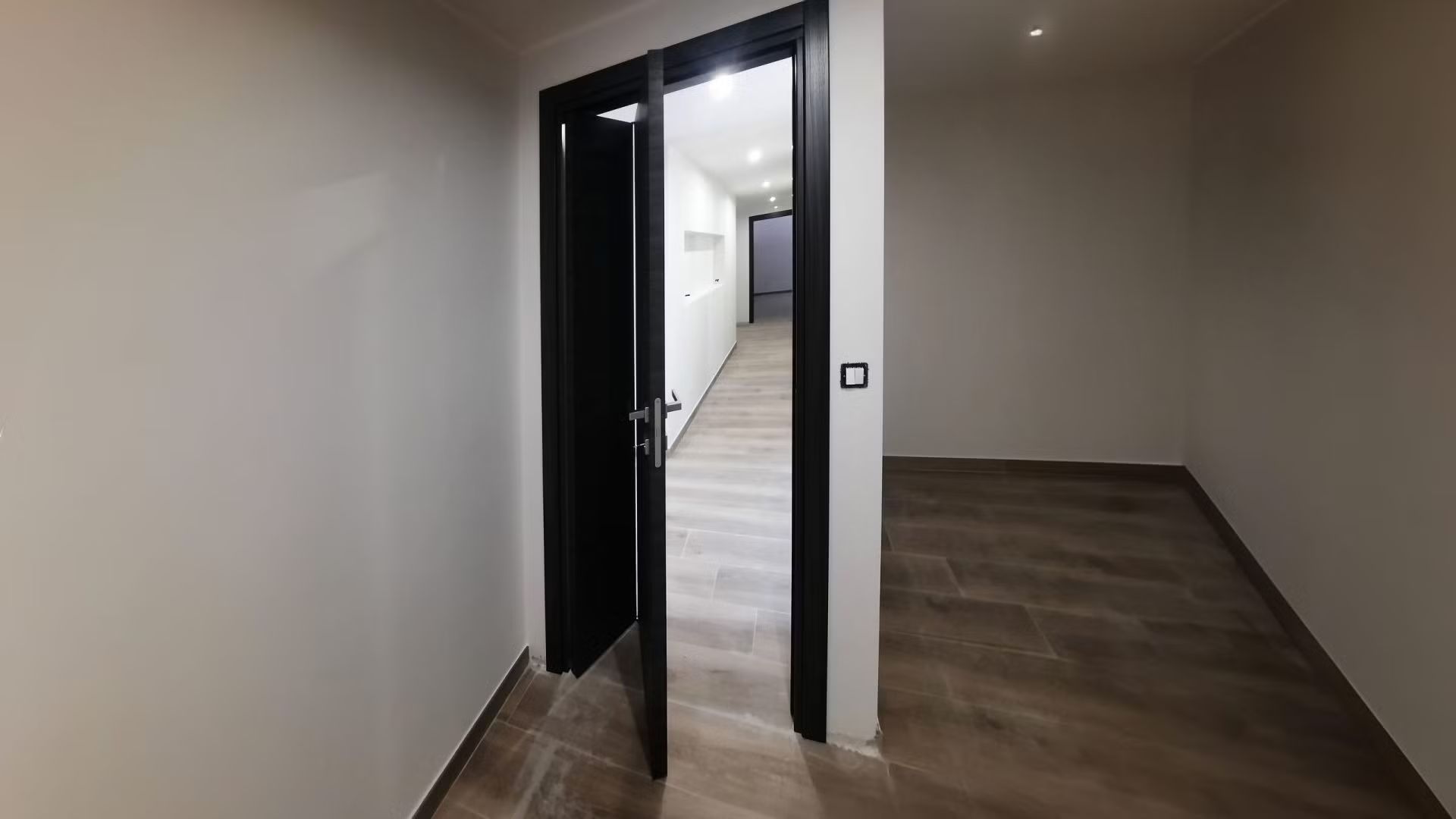 Una stanza vuota con una porta nera e un pavimento di legno.