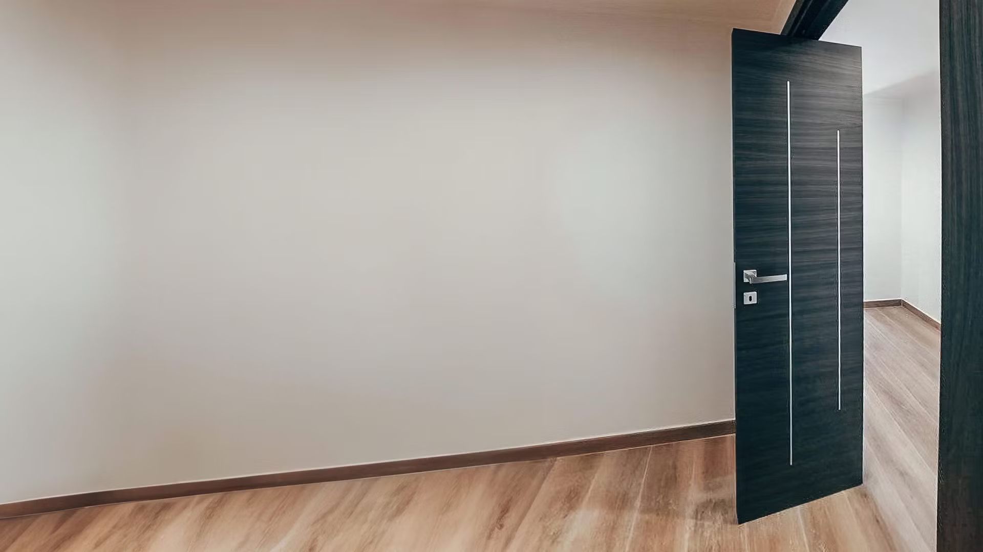 Una stanza vuota con un pavimento in legno e una porta nera.