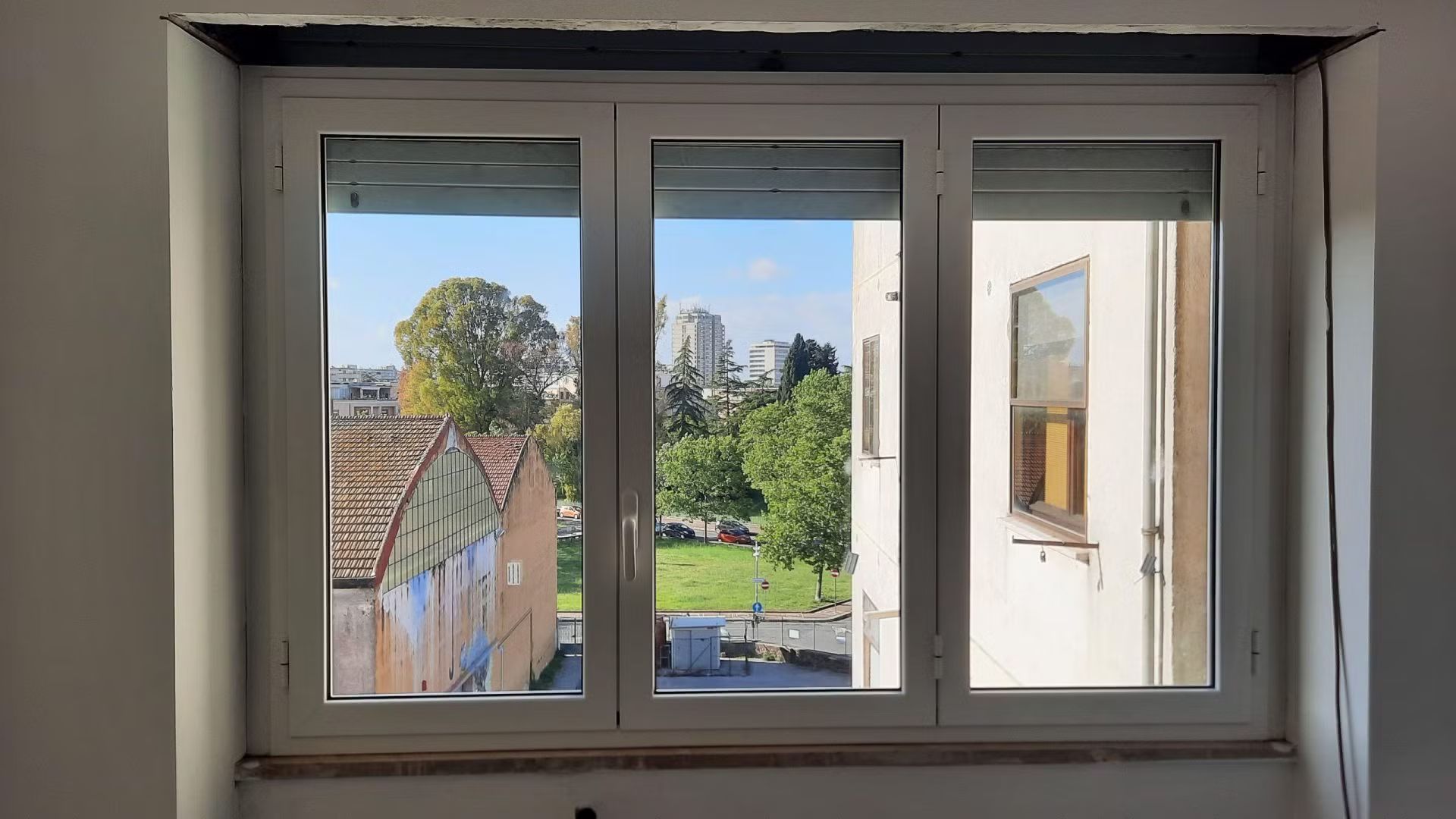 Una finestra bianca con vista su un edificio e sugli alberi.