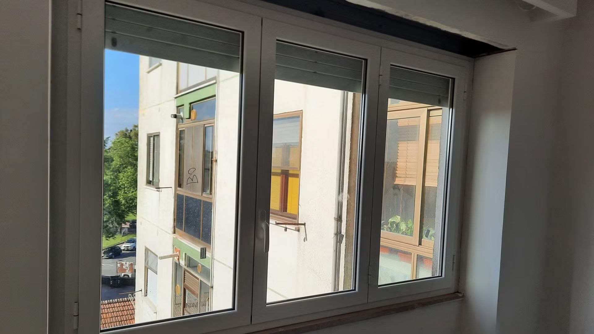 Una stanza con tre finestre e vista su un edificio.