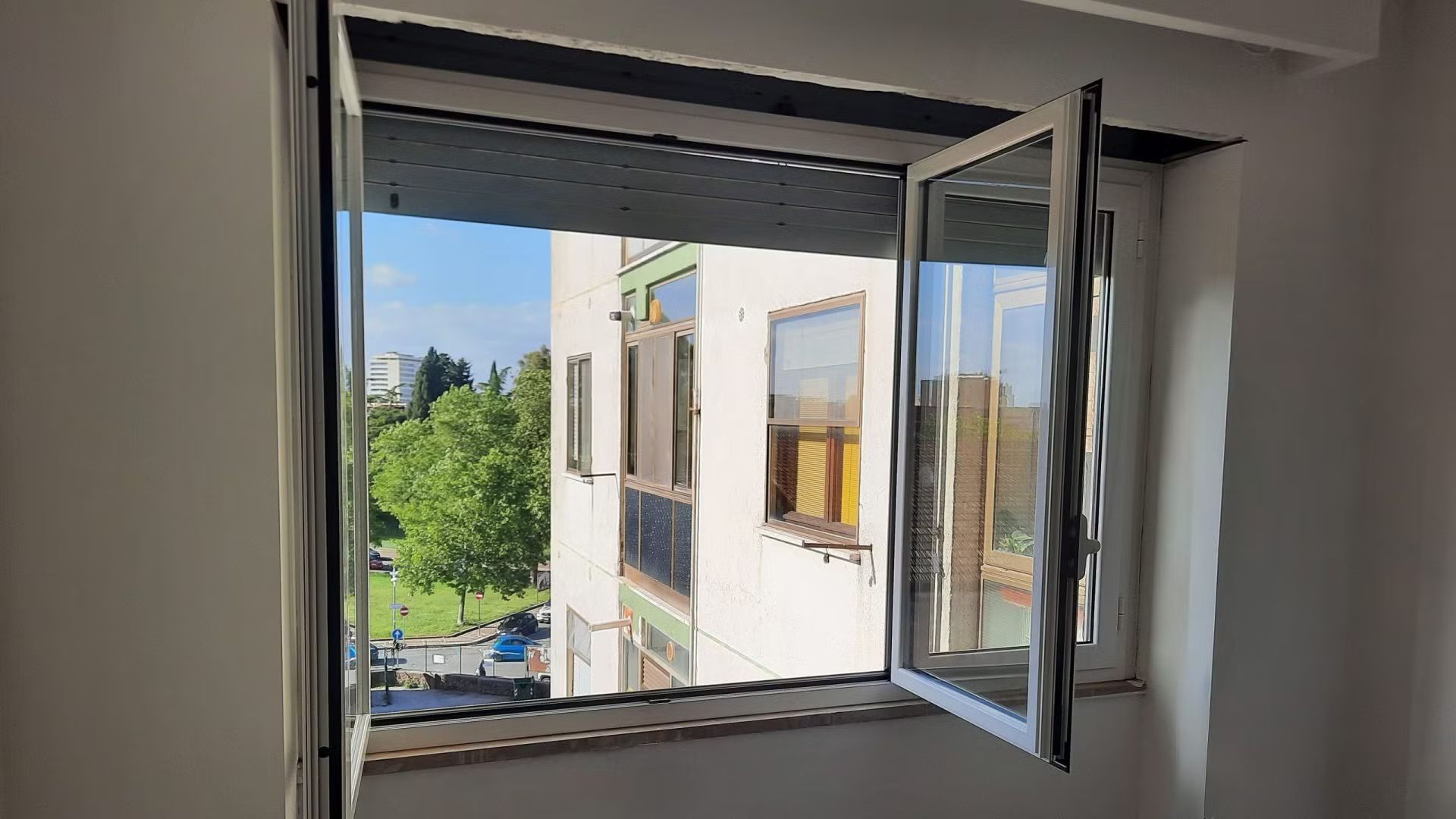 Una stanza con una finestra aperta e vista su un edificio.