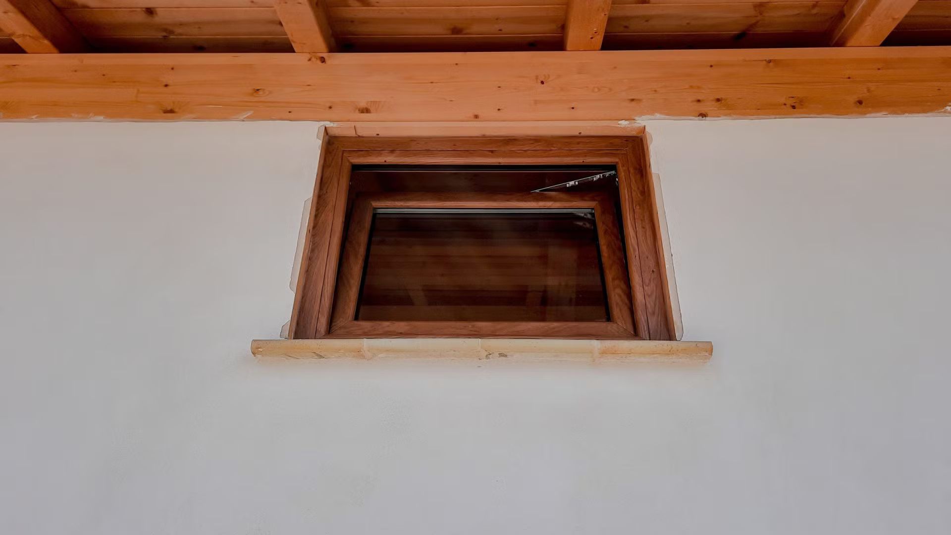 Una finestra di legno in un muro bianco con un tetto di legno.