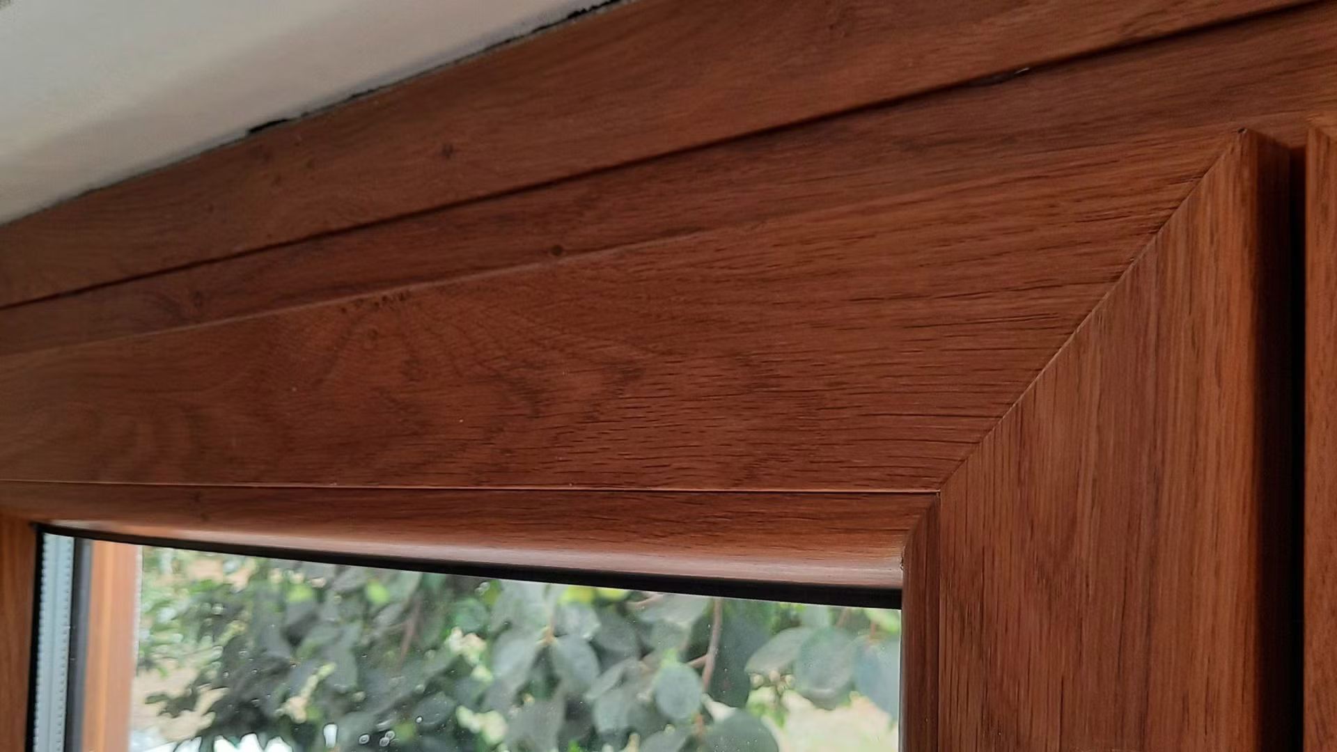 Un primo piano del telaio di una finestra in legno con un albero sullo sfondo.