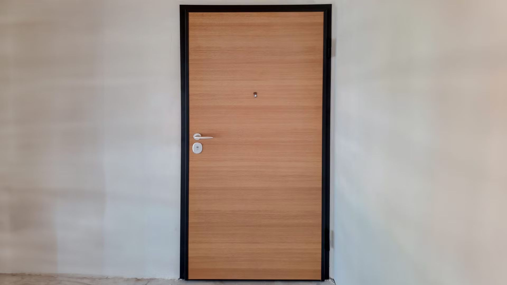 Una porta di legno con una cornice nera è appesa a una parete bianca.