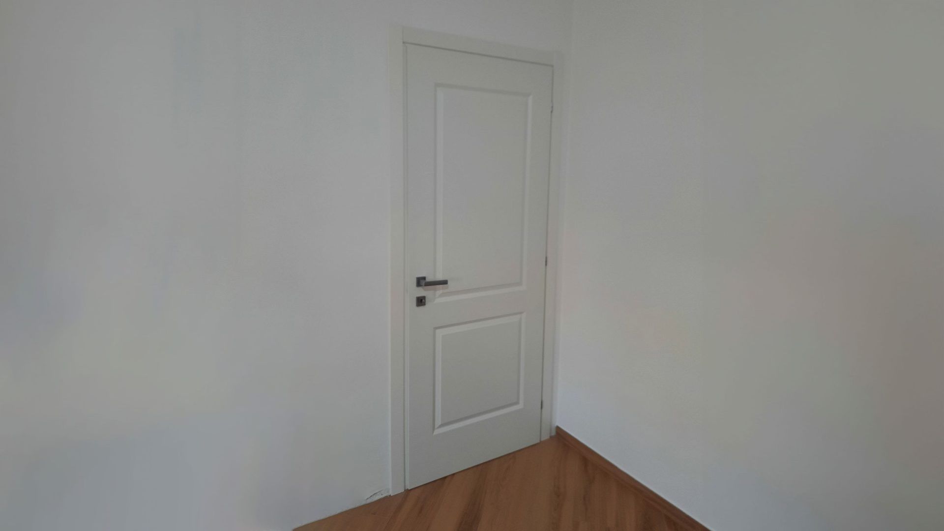 Una stanza vuota con una porta bianca e un pavimento in legno.