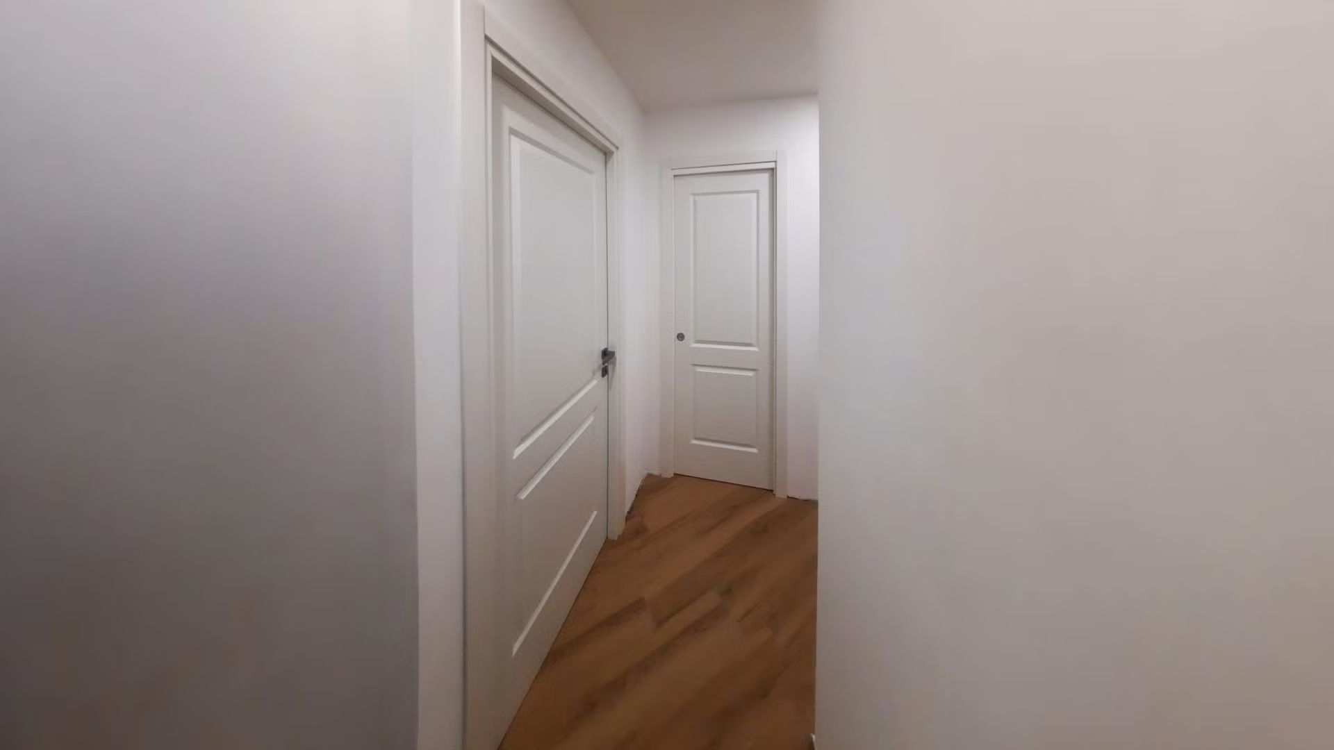 Un corridoio con porte bianche e pavimenti in legno in una casa.