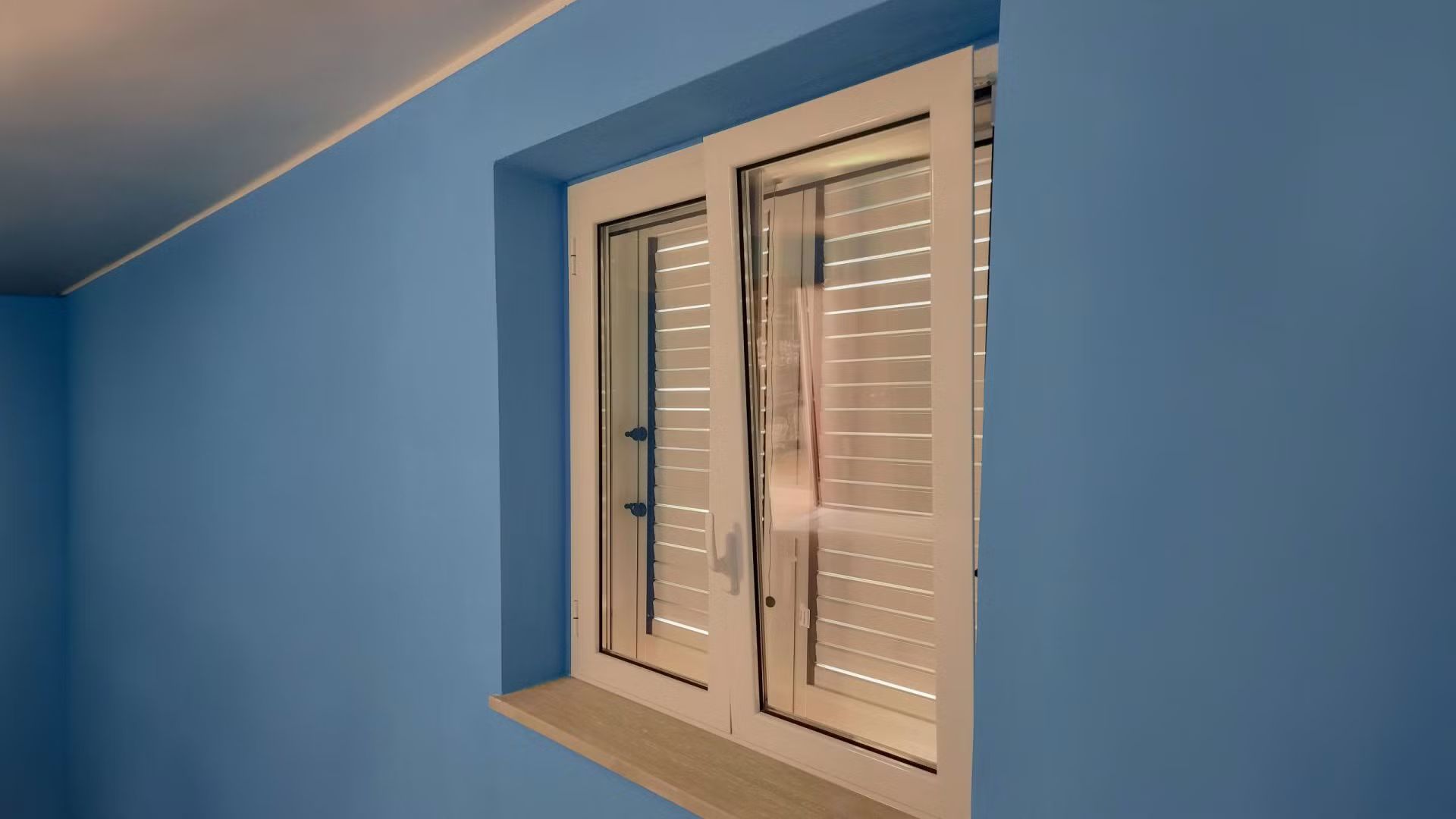 Una finestra bianca con le persiane in una stanza blu.