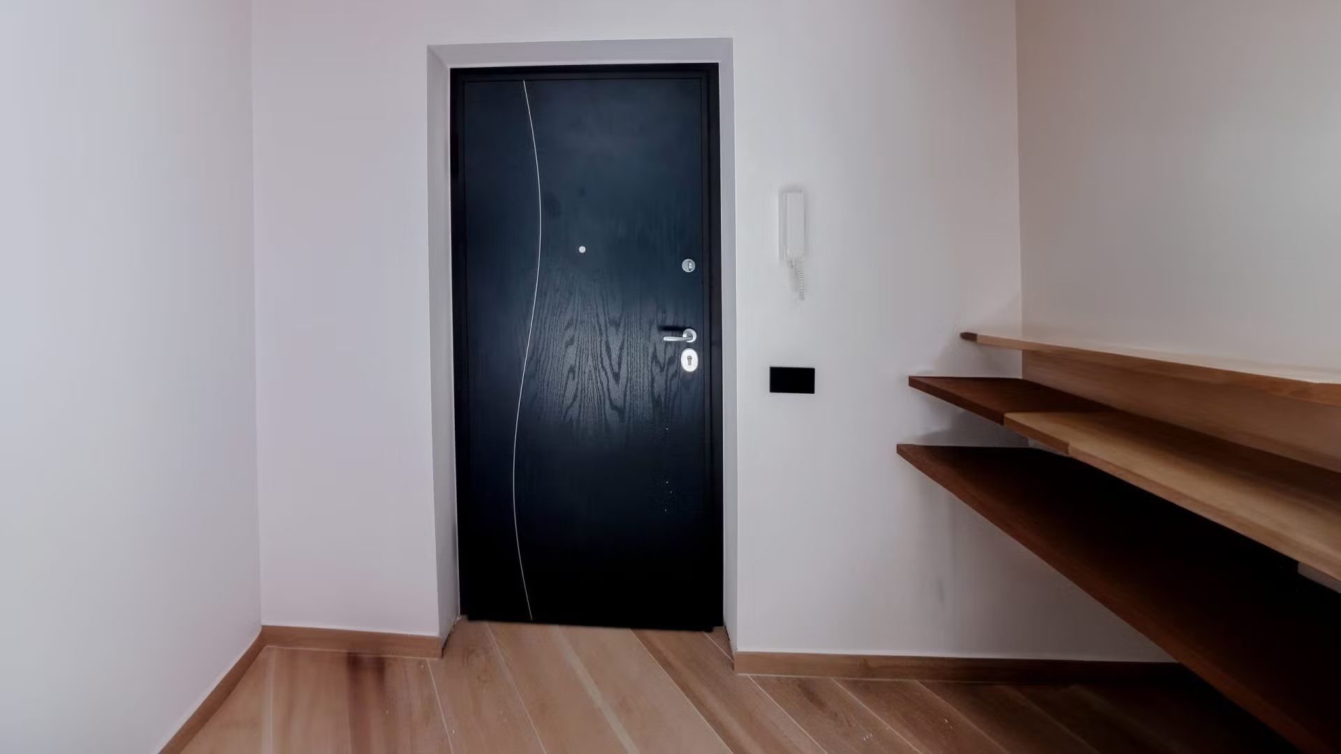 Una stanza vuota con una porta nera e scaffali di legno.