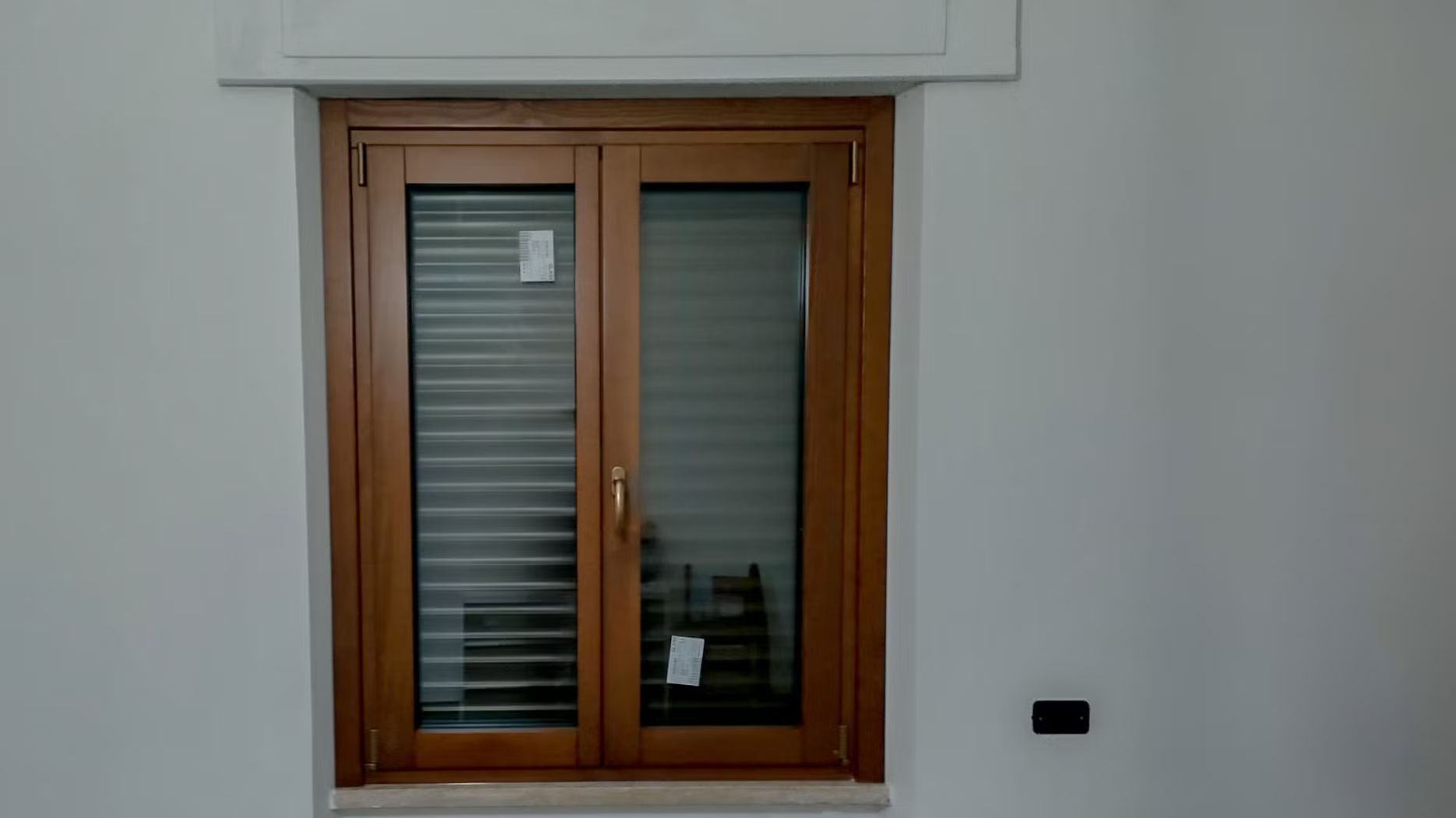 Una finestra di legno con persiane si trova su una parete bianca.