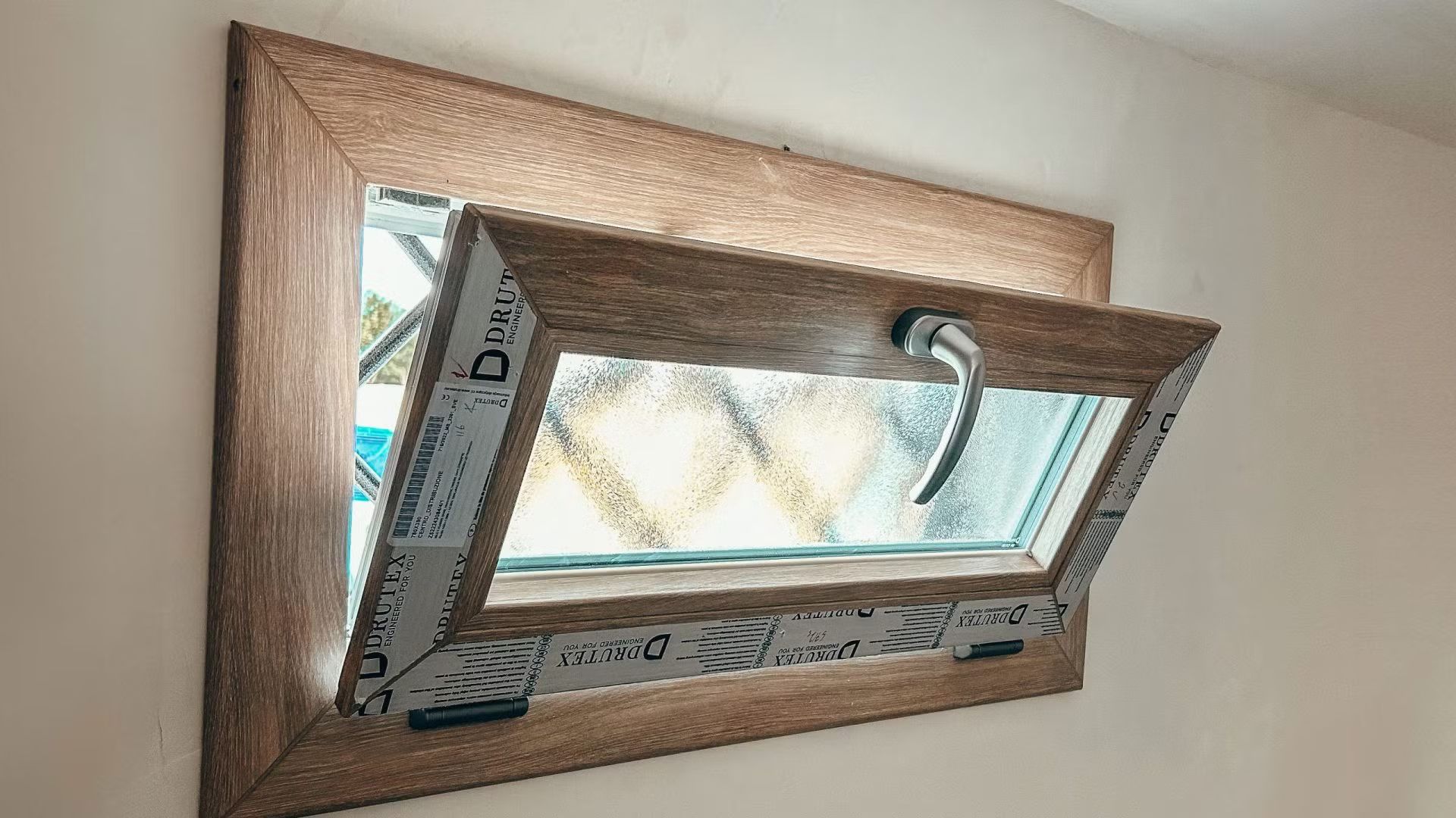 Una finestra con una cornice di legno è appesa a una parete bianca.