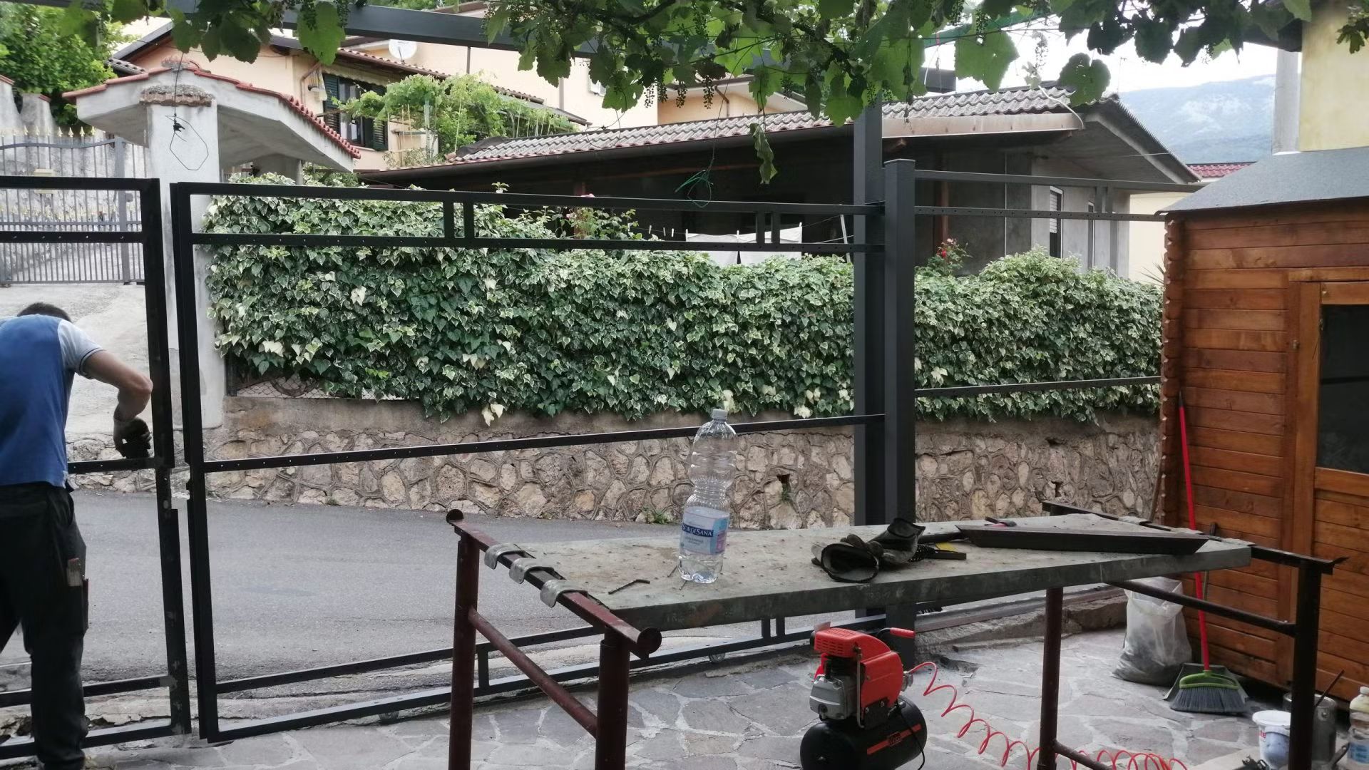 Un uomo sta lavorando su un cancello di metallo davanti a una baracca di legno.