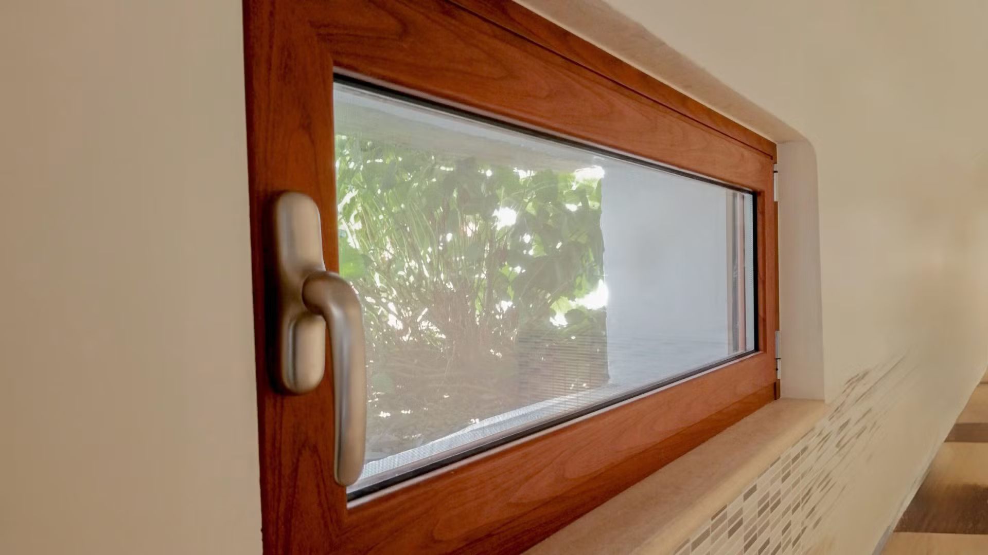 Una finestra di legno con una maniglia bianca si trova su una parete bianca.