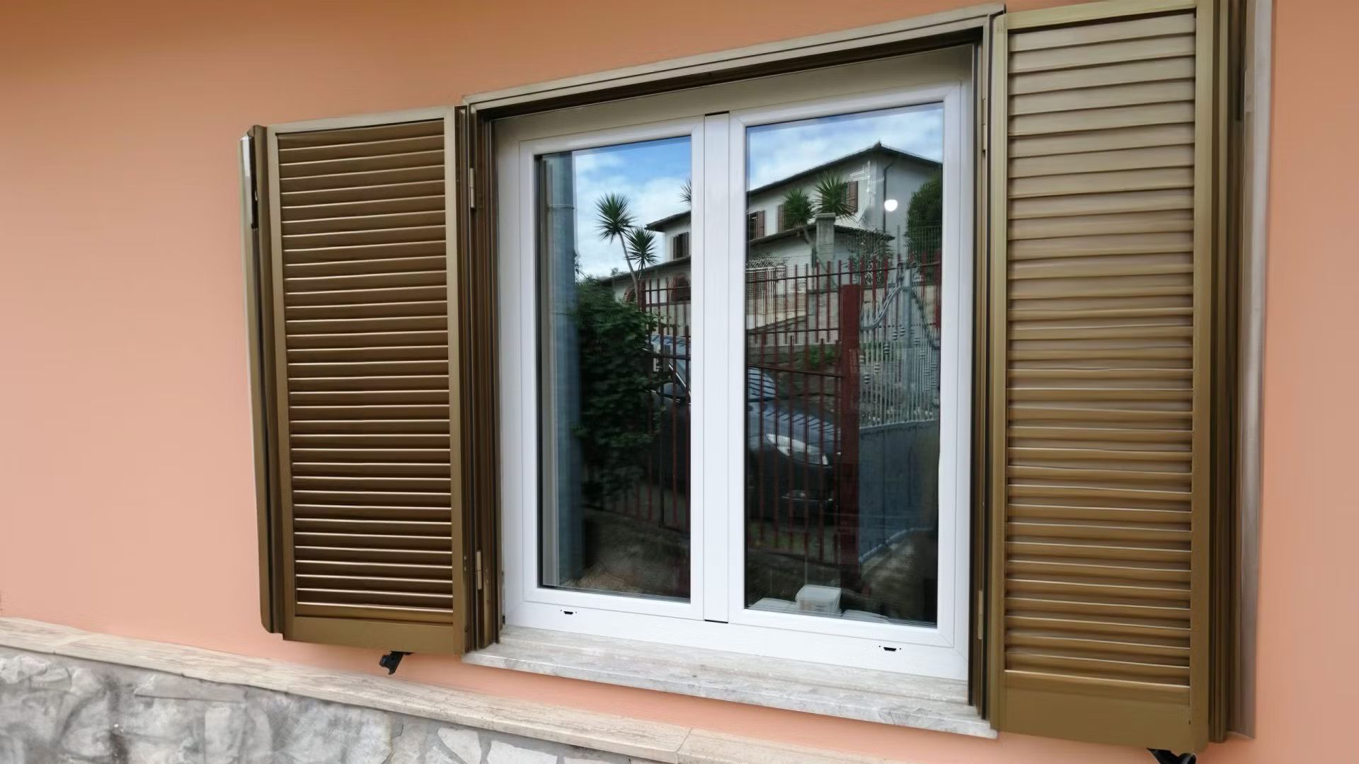 Una finestra bianca con persiane marroni su una parete rosa.