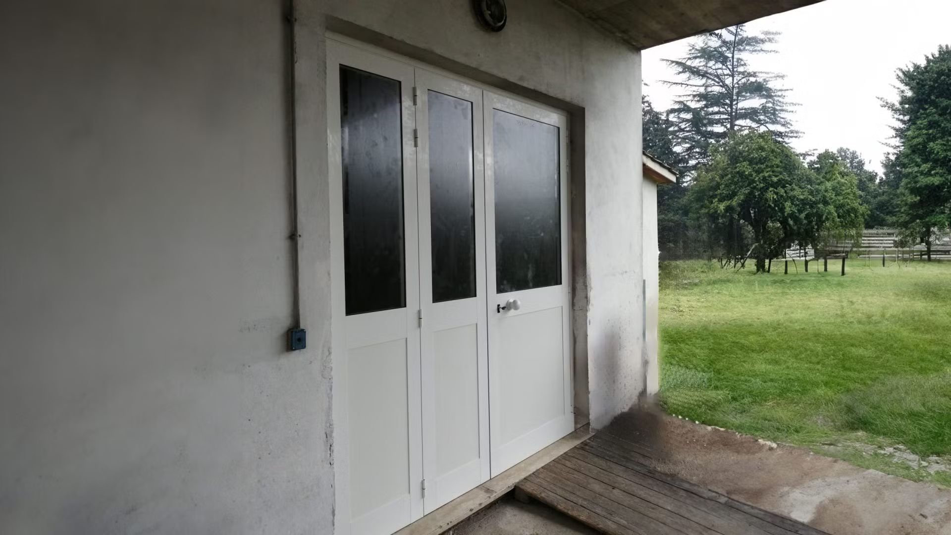 Una porta da garage bianca con finestre nere è aperta su un campo erboso.