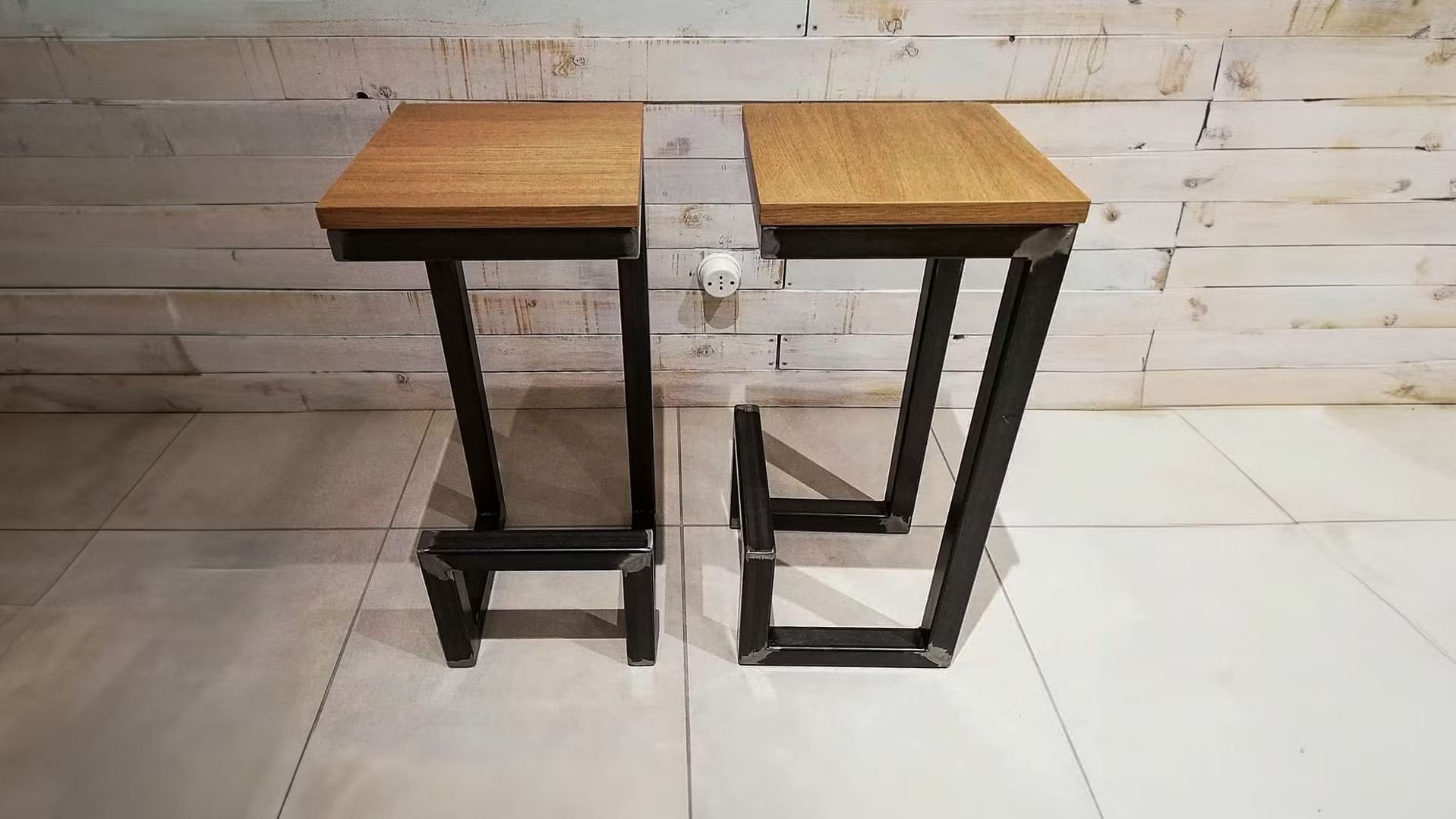 Due sgabelli di legno sono appoggiati su un pavimento piastrellato di fronte a un muro di mattoni.