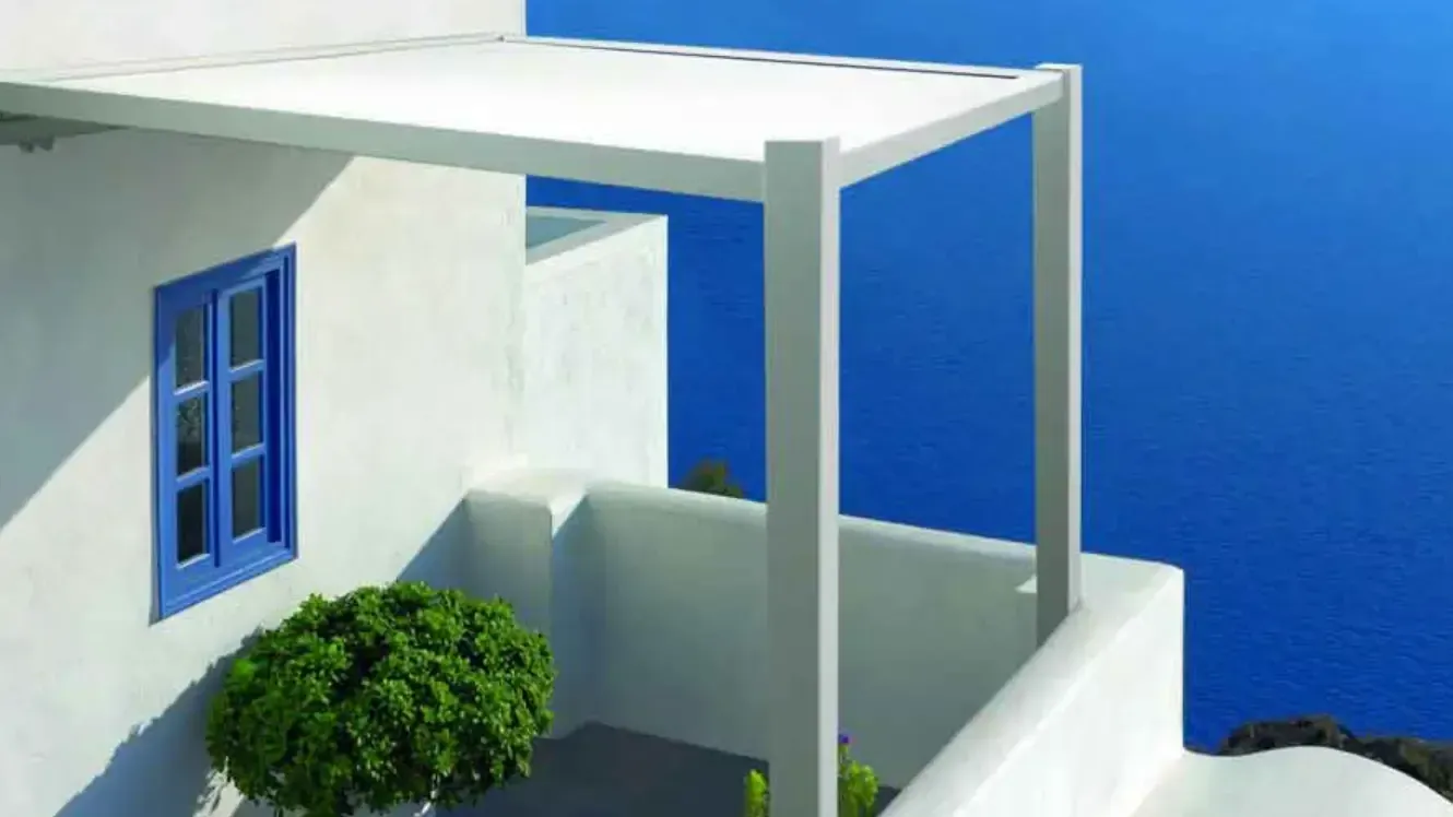 Una casa bianca con una finestra blu e un pergolato che si affaccia sull'oceano.