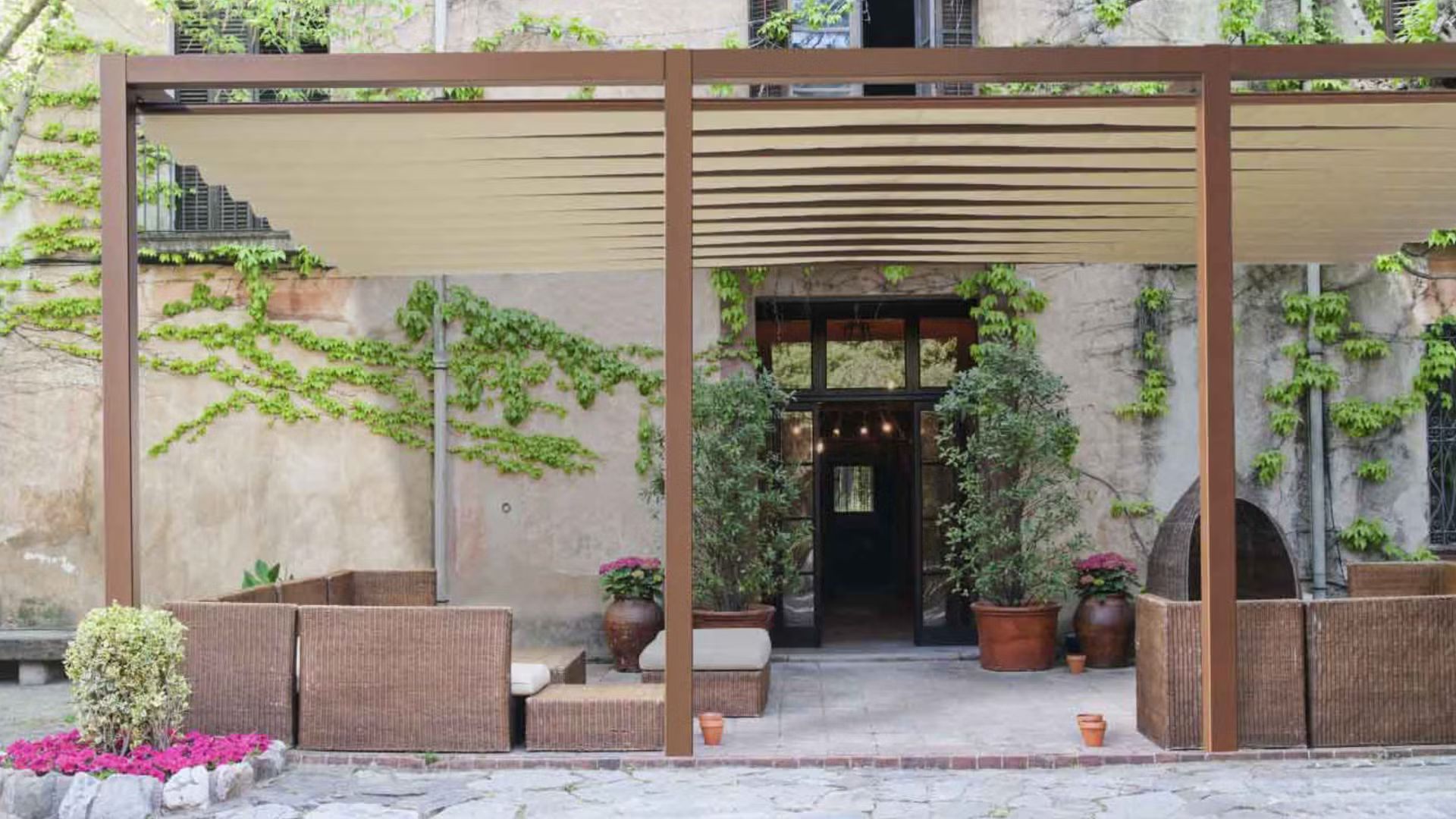 Un patio con pergolato e mobili in vimini di fronte a un edificio.