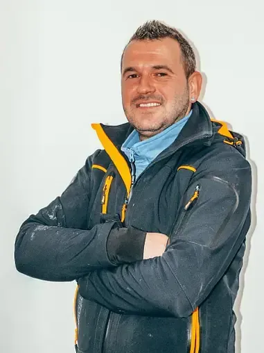 Un uomo con una giacca blu e gialla è in piedi con le braccia incrociate.