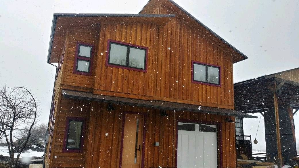 A wooden house with a garage door is covered in snow.
