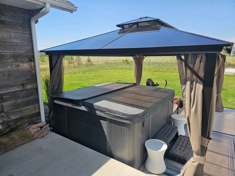 A hot tub is sitting under a gazebo on a patio.