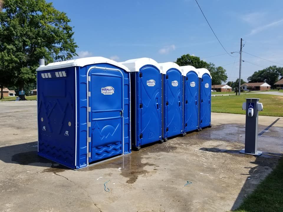 A row of blue portable toilets with white tops on a gravel surface, outdoors. A row of blue portable toilets with white tops on a gravel surface, outdoors.