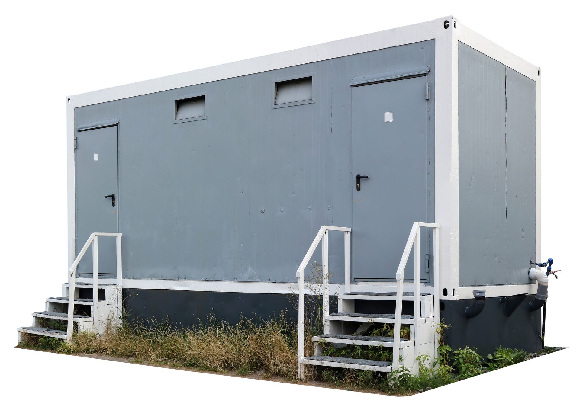 A gray portable restroom trailer placed in a public space, featuring two white stairs and doors.