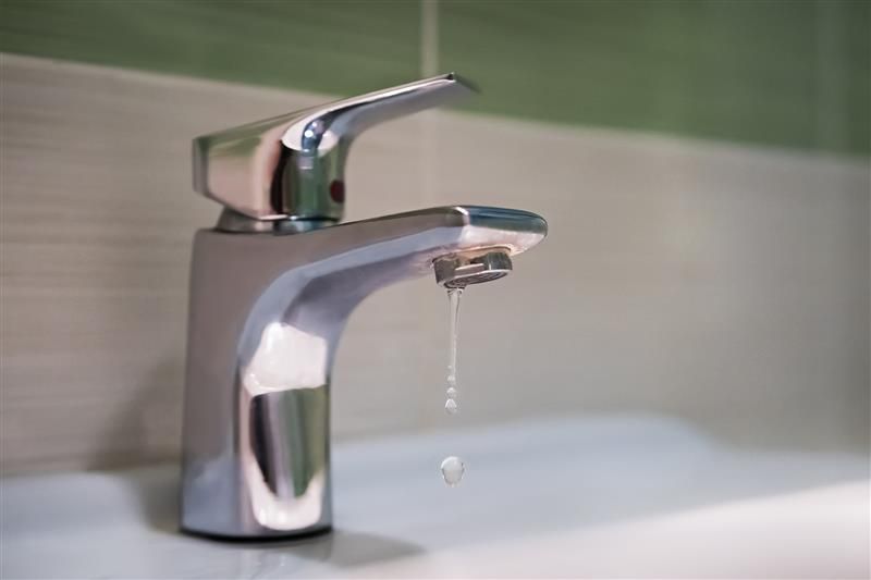 Close-up of a silver tap, while water drips from it, inside a bathroom trailer.