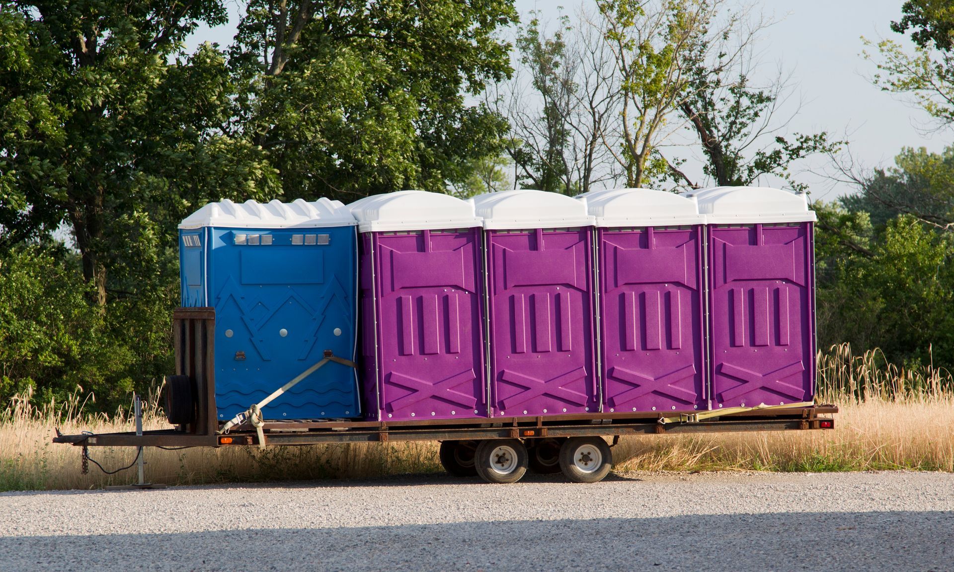 A set of blue and purple porta potty toilets on a trailer ready to be shipped to an event.