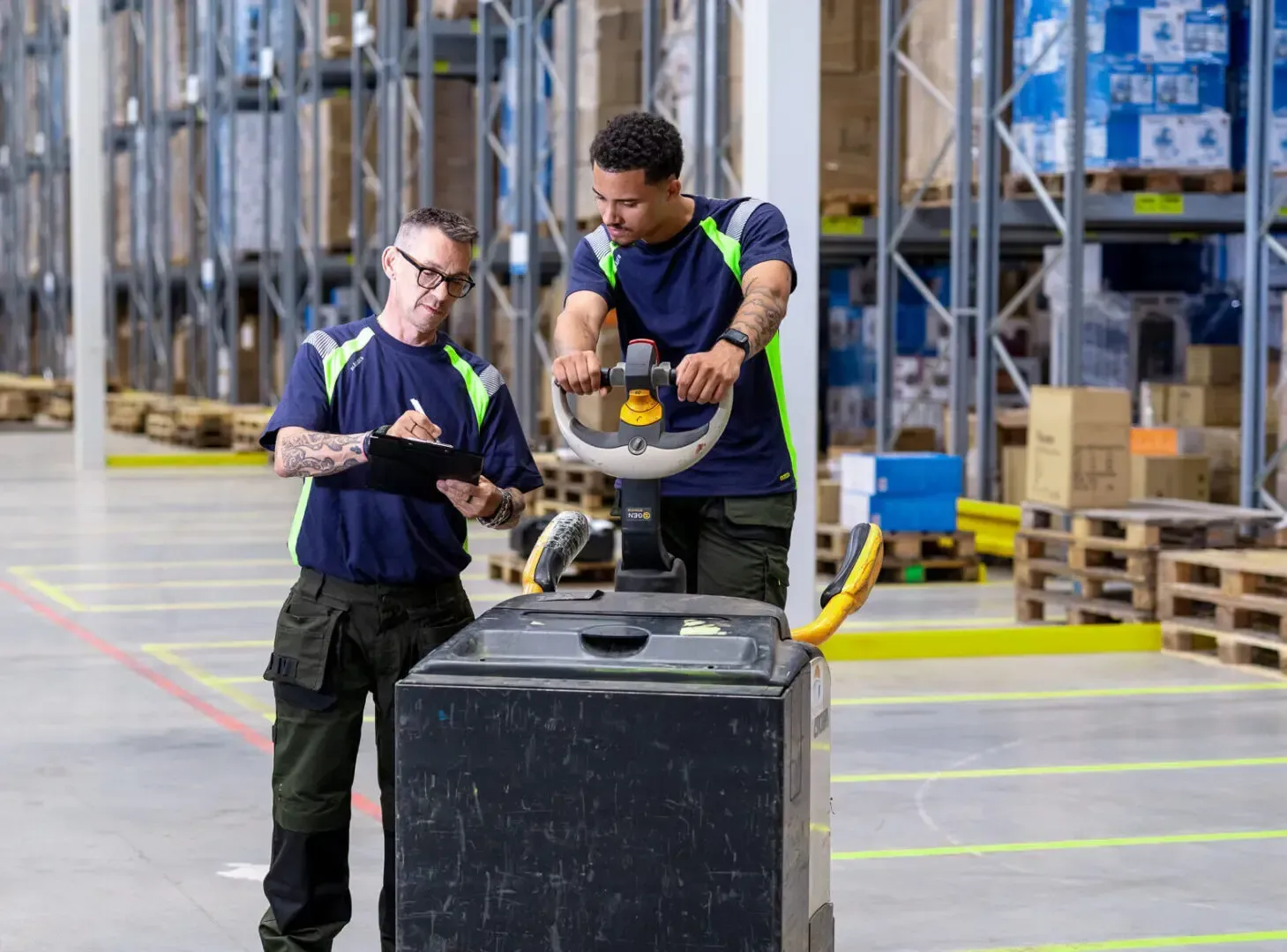 Two men are standing next to each other in a warehouse looking at a clipboard.