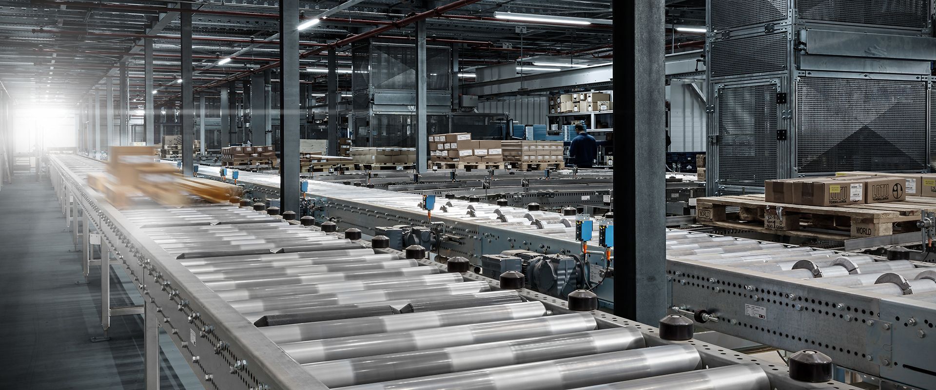 Een lopende band in een magazijn vol met dozen en pallets.
