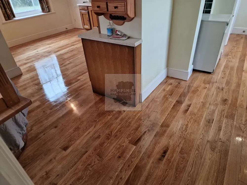 Wooden floor in a room, reflecting light from a window. A small wooden cabinet is in the middle.