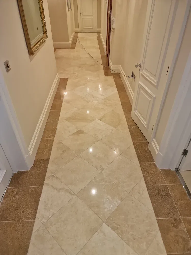 Hallway with light beige and brown tile flooring, leading to a doorway and light walls.