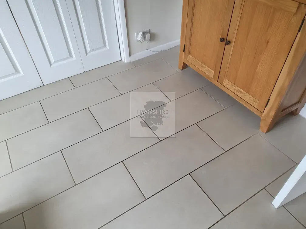 Tan rectangular floor tiles in a room with a wooden cabinet and white doors.
