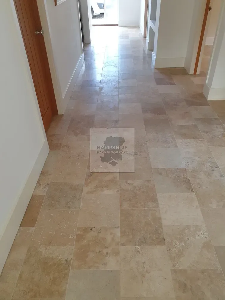 Hallway with light beige stone tile floor. White trim and walls. A wooden door is on the left.