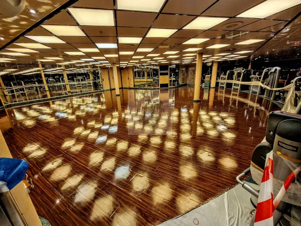 Gym interior with reflective wooden floor and bright ceiling lights.