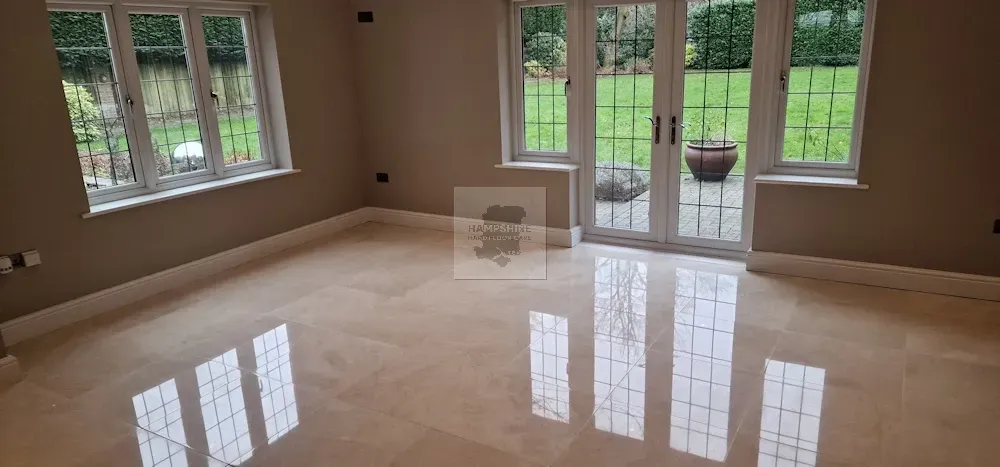 A room with windows and glass doors, a polished light-colored floor, and beige walls.