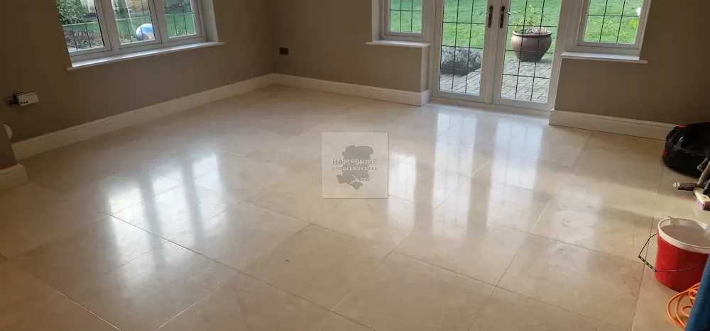 Room with polished light-colored tiled floor, windows, and french doors. Neutral walls with white baseboards.