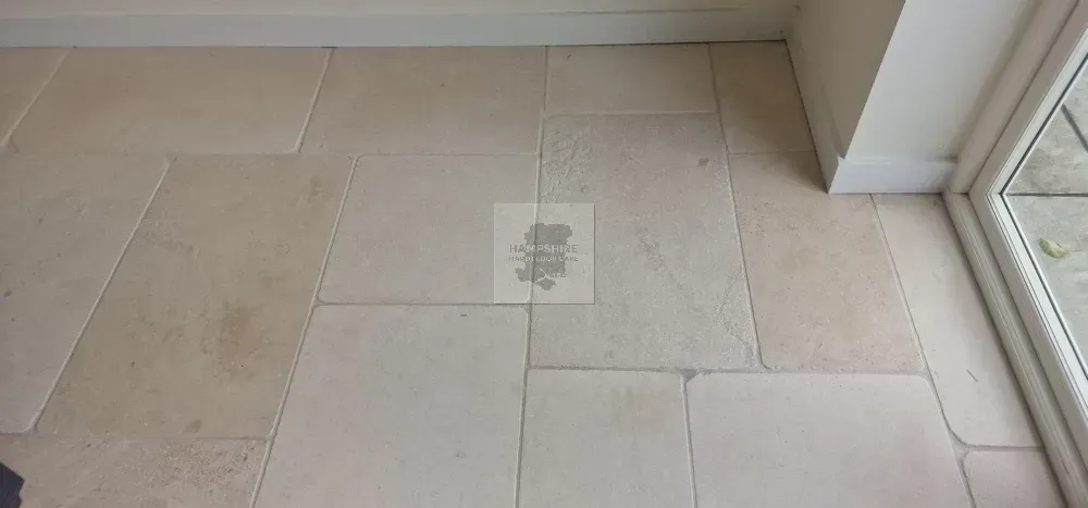 Beige stone tile floor in a room, with white wall trim and a window frame.