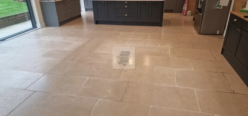 Tan stone tiled kitchen floor with dark cabinets and a large window.