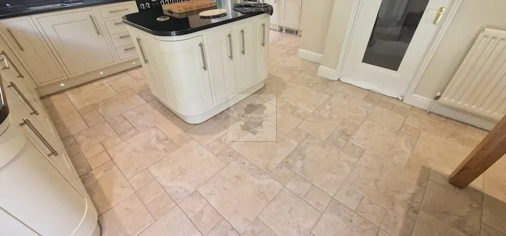 Kitchen with cream cabinets, dark countertop island, and light-colored stone tile floor.