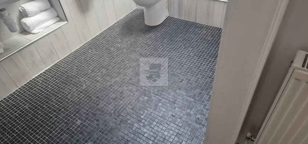 Bathroom floor tiled with small dark square tiles. A white toilet is visible. White towels are stored in a recessed shelf.