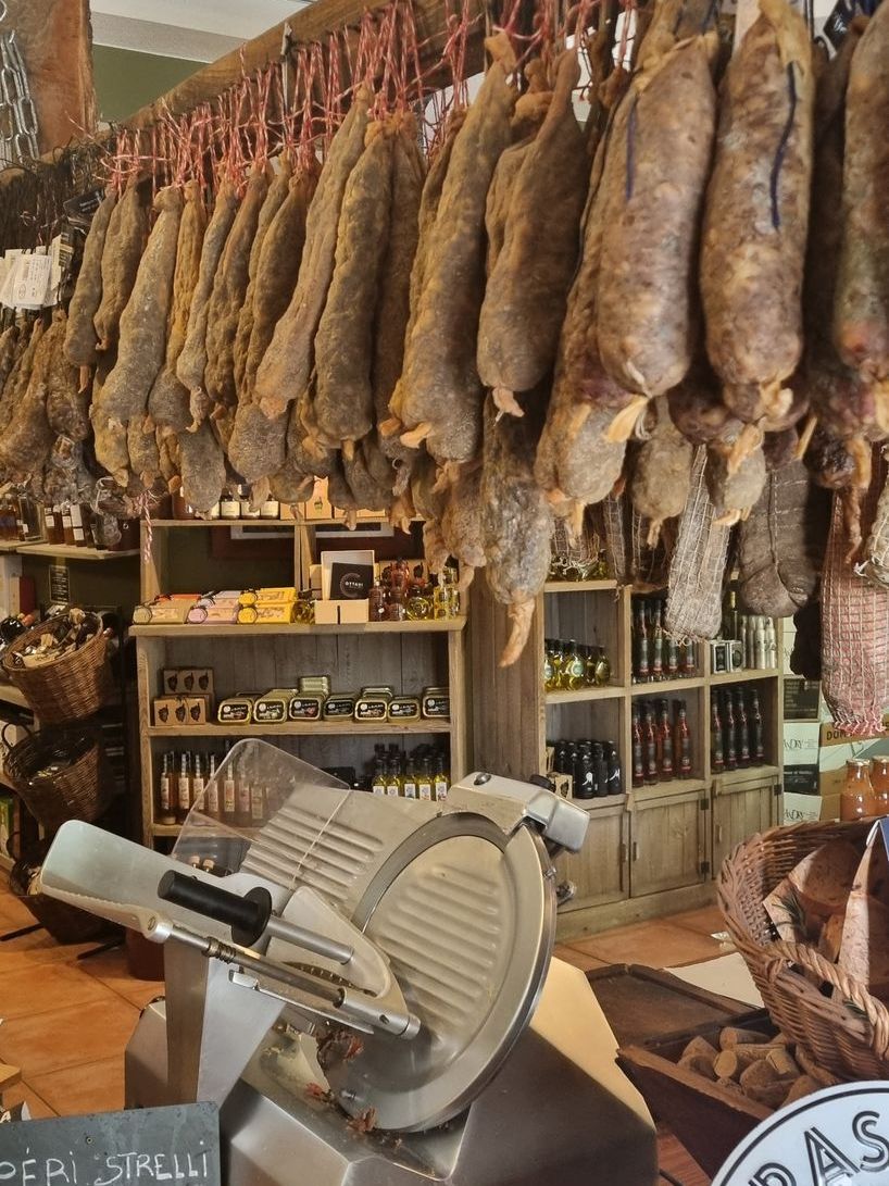 A meat slicer is sitting in front of a wall of meat