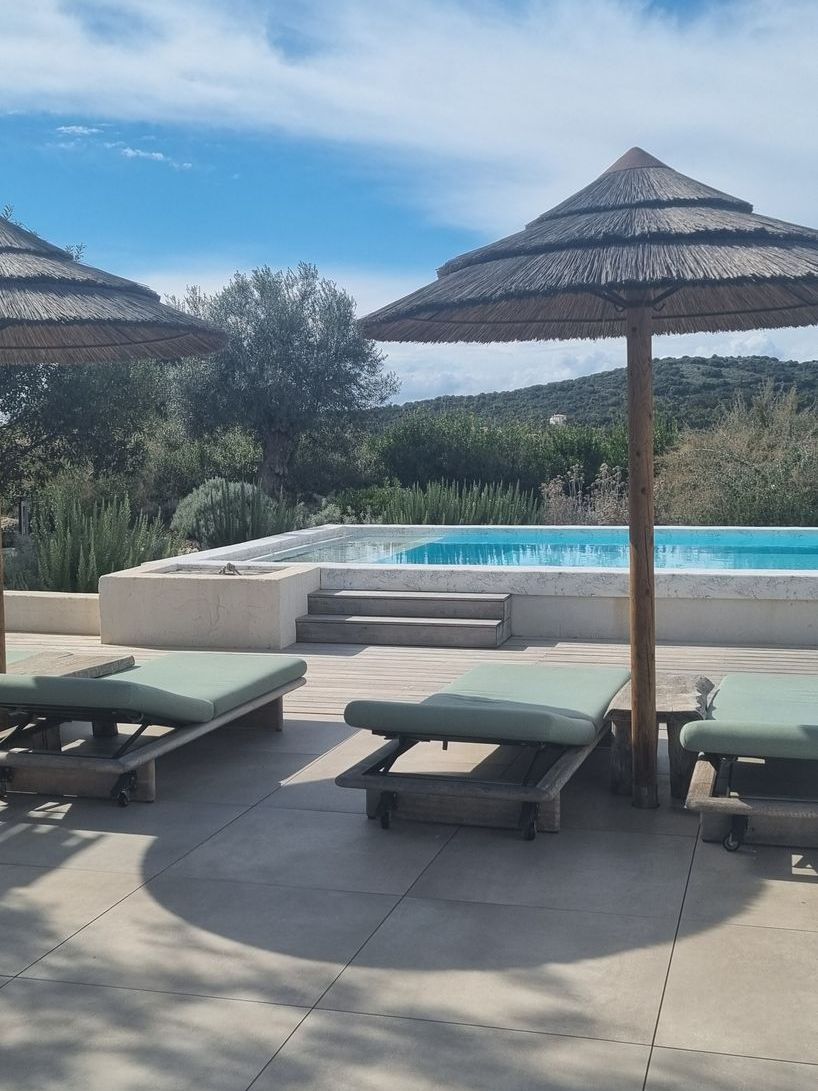 A patio with chairs and umbrellas next to a swimming pool.