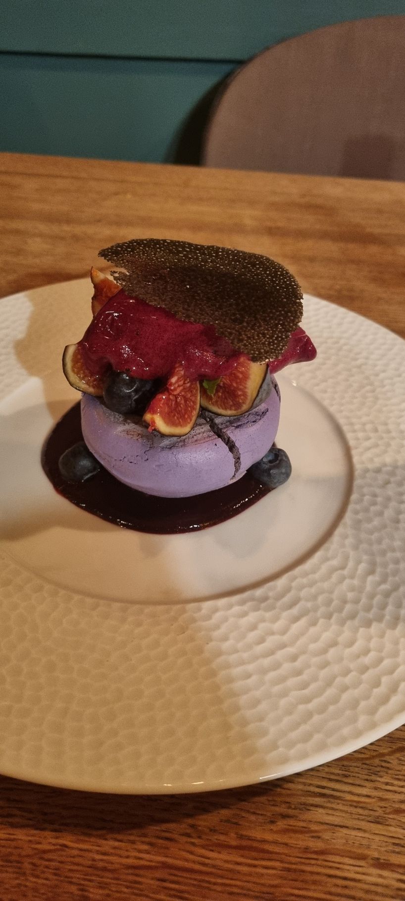 A white plate topped with a purple dessert and berries on a wooden table.