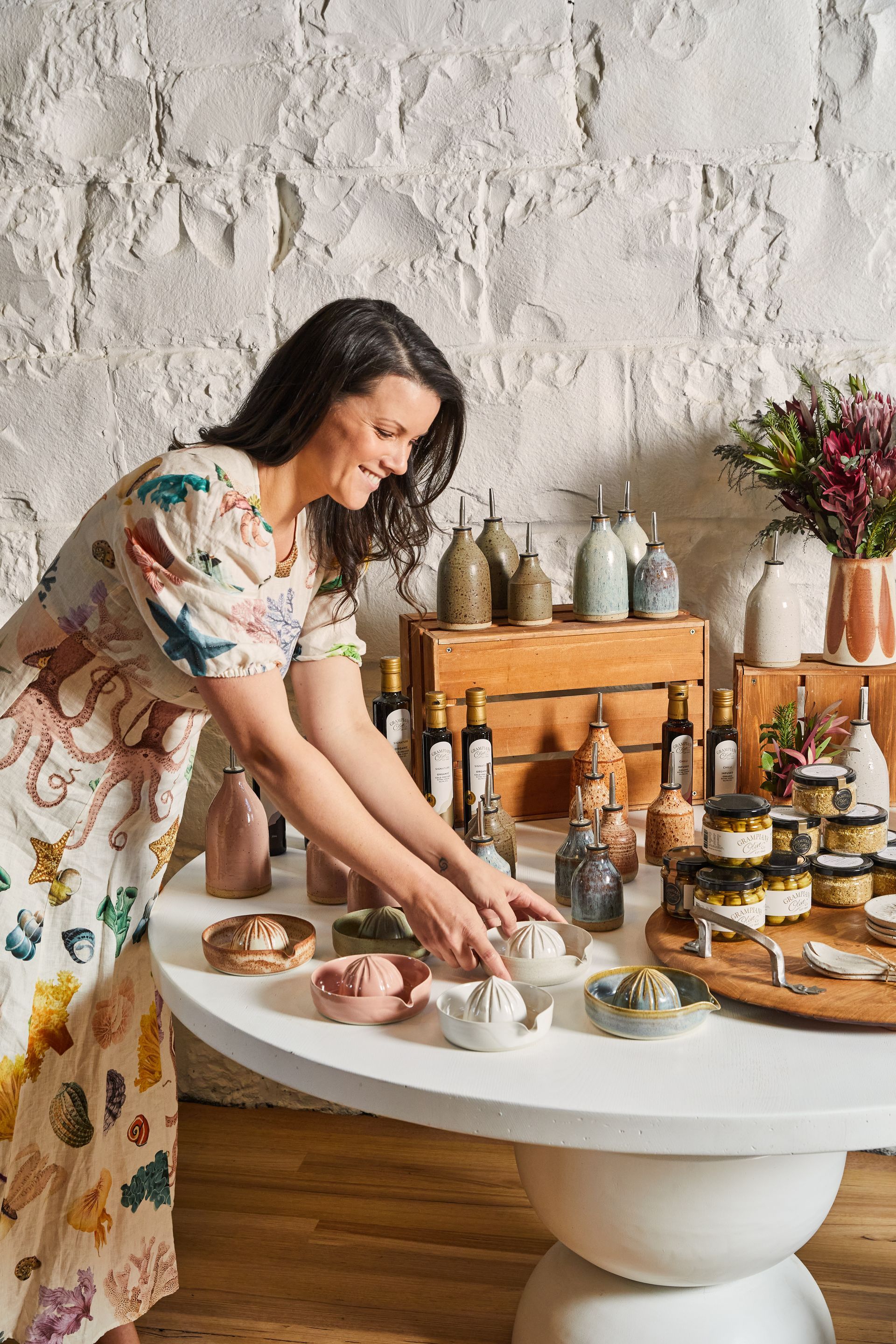 A woman in a dress is standing in front of a shelf filled with ceramics.