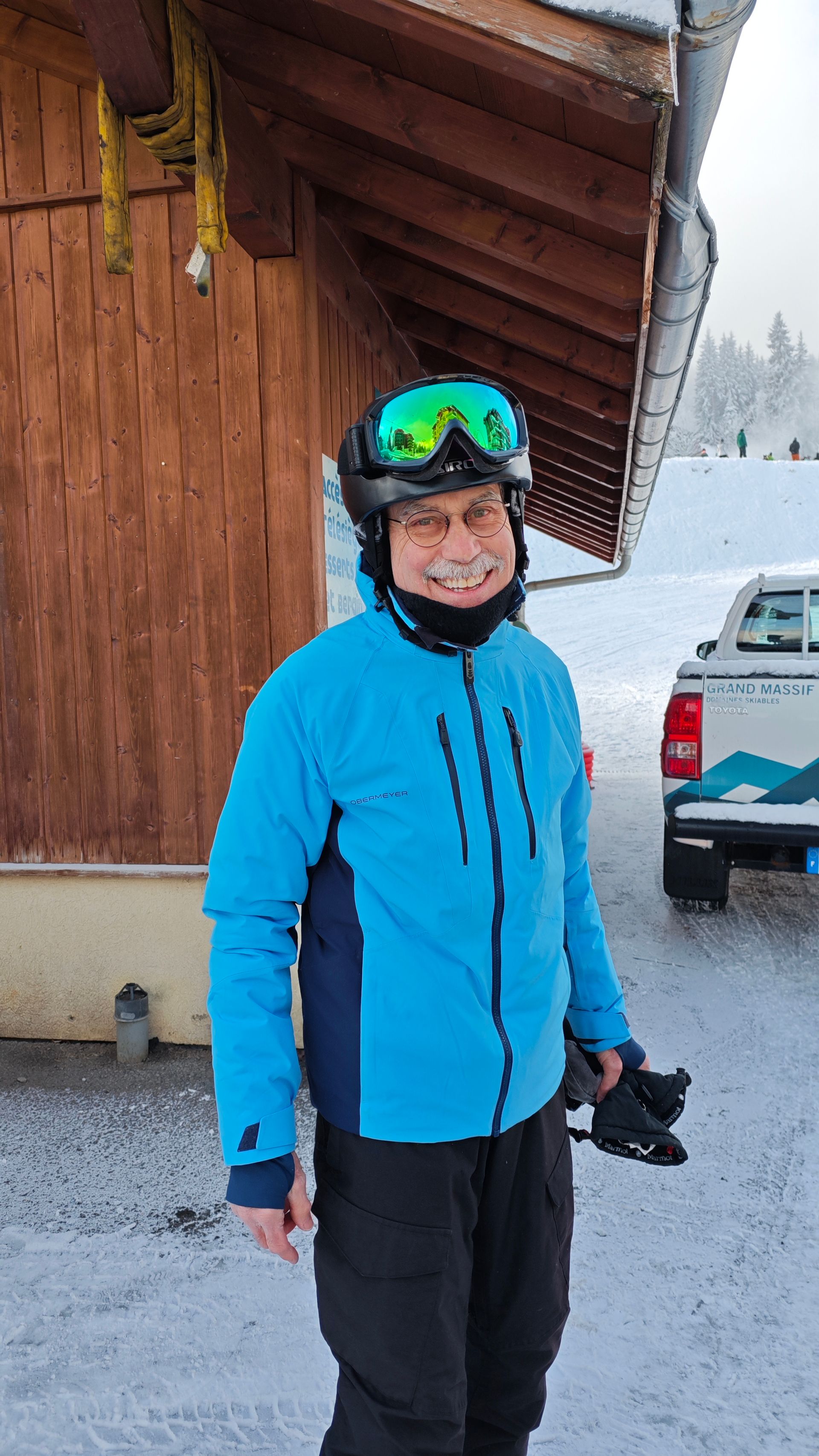 A man wearing a blue jacket and goggles is standing in the snow.